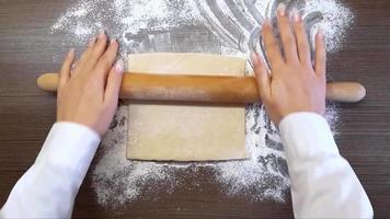 Women's hands roll out the dough with a wooden rolling pin, on the surface of the table. The view from the top video