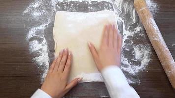 Women's hands roll out the dough with a wooden rolling pin, on the surface of the table. The view from the top video