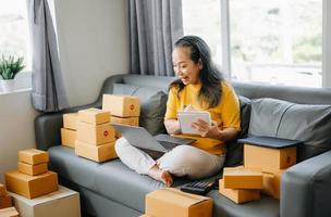 Startup small business SME, Entrepreneur owner Senior woman using smartphone or tablet taking receive and checking online purchase shopping order to preparing pack product box. photo