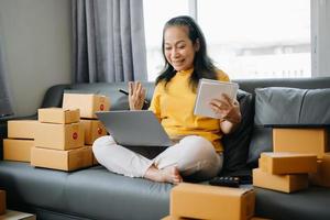 Startup small business SME, Entrepreneur owner Senior woman using smartphone or tablet taking receive and checking online purchase shopping order to preparing pack product box. photo