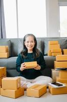 Startup small business SME, Senior woman hand using smartphone or tablet taking receive and checking online purchase shopping order to preparing pack product box. business online shopping concept photo