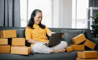 Senior business owner woman prepare parcel box and standing check online orders for deliver to customer on tablet, laptop Shopping Online concept. photo