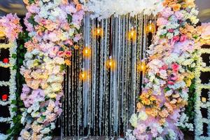 Colorful artificial flowers with Decorative antique Edison style filament light bulbs hanging on wedding stage decoration. photo