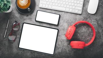 Modern office desk workplace with blank screen smart phone and tablet, keyboard computer, mouse, pen, eyeglass and cup of coffee, Top view flat lay. photo