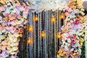 Colorful artificial flowers with Decorative antique Edison style filament light bulbs hanging on wedding stage decoration. photo