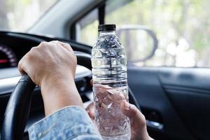Asian woman driver hold cold water for drink in car, dangerous and risk an accident. photo