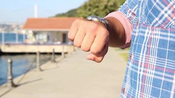 Jeune homme attendre et vérification temps sur le sien montre, en marchant sur bord de mer, sélectif se concentrer, bruit effet video