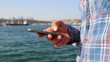 Person use smartphone on seaside, a sea view with a ship, a sunny day, selective focus, noise effect video