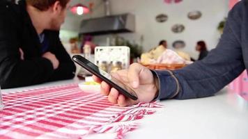 persona uso smartphone, controllo Telefono, mentre in attesa cibo, selettivo messa a fuoco, rumore effetto video