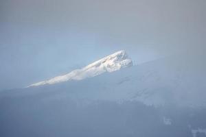 Scenic view of snow covered mountain peak seen through fog photo