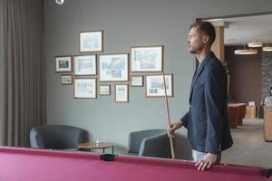 Thoughtful man holding snooker stick standing in luxury hotel photo