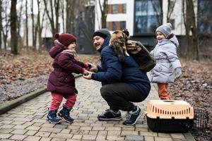 padre e hijas con gato en carro de jaula de plástico para mascotas de viaje al aire libre en el parque. foto