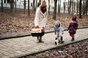 Mother and daughters walking with kitten in travel plastic cage carriage outdoor at park. photo