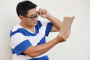 un hombre asiático de mediana edad usa anteojos y está leyendo un libro. concepto, problema de la vista. optometría. anteojos con lentes convexas o cóncavas. miopía.enfermedad ocular foto