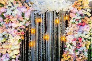 Colorful artificial flowers with Decorative antique Edison style filament light bulbs hanging on wedding stage decoration. photo