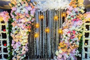 Colorful artificial flowers with Decorative antique Edison style filament light bulbs hanging on wedding stage decoration. photo