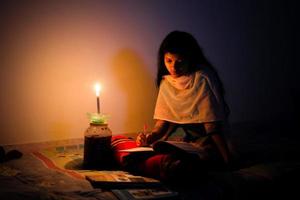 un joven niña estudiando a hogar con luz de una vela después electricidad carga derramamiento a dhaka ciudad. foto