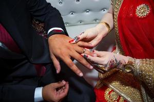 A bride is wearing a ring on the groom's finger. Indian Wedding. photo