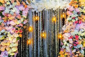 Colorful artificial flowers with Decorative antique Edison style filament light bulbs hanging on wedding stage decoration. photo