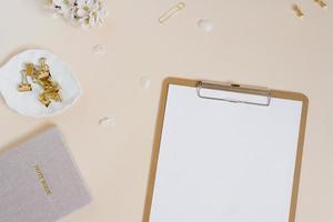 escritorio femenino o blogger estilizado, escritorio de oficina. lugar de trabajo, flores blancas de un manzano, cuaderno, bolígrafo, clips de papel y una tableta con una hoja de papel en blanco sobre un fondo beige foto