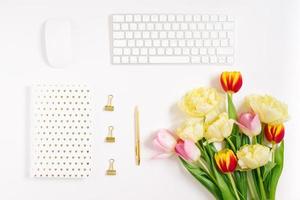 Spring flat lay blogger or freelancer. White notepad, pen, bouquet of tulips, keyboard, mouse and paper clips on a white background with copy space photo