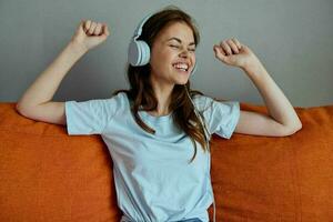 beautiful woman listening to music with headphones on the orange sofa apartments photo