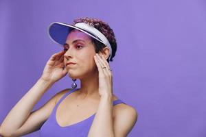 Portrait of a sporty fashion woman posing smiling in a purple sports suit for yoga and a transparent cap on a purple background monochrome photo