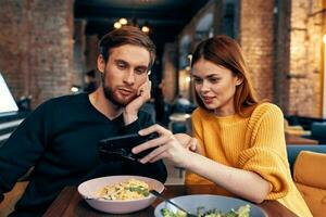 a woman in a sweater with a mobile phone and a guy with a beard are sitting in a restaurant photo