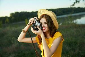 mujer fotógrafo en sombrero mirando dentro el cámara lente sonrisa naturaleza pasatiempo foto