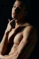 handsome athlete on a black background holds his hand near the face pumped muscles biceps model photo