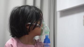 liten asiatisk flicka har ett syre mask och andas genom en nebulisator på de sjukhus. begrepp av bronkit, respiratorisk och medicinsk behandling. video