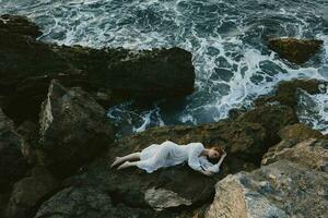 woman in long white dress wet hair lying on a rocky cliff nature landscape photo