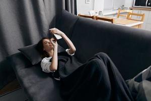 young woman covered with a blanket lies on the couch with a mobile phone in her hand top view photo