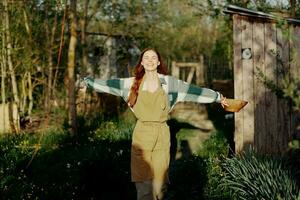 mujer camina felizmente mediante jardín con pájaro alimentador después alimentación pollos en su granja foto