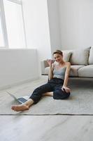 Freelance woman with laptop and phone works from home sitting on the floor in her home clothes with a short haircut, free copy space photo