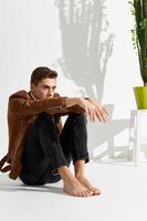 Handsome young man sits on the floor In a bright room and a flower in a pot photo