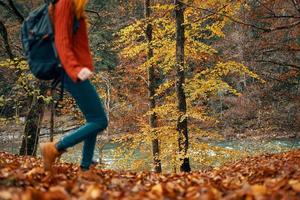 young woman in jeans and a sweater with a backpack on her back walks in the park in autumn in nature, bottom view photo