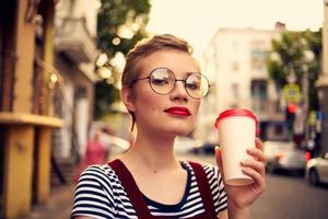 bonito mujer con corto peludo lentes al aire libre un taza de bebida foto