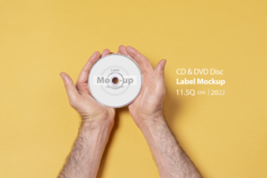 Male hand holding a CD-DVD by two hands in front of yellow background psd