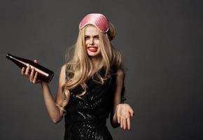 Woman holding a bottle with alcohol in her hands on a gray background black dress sleep mask photo