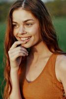 Close-up portrait of a smiling young woman in the sun with red hair in nature photo