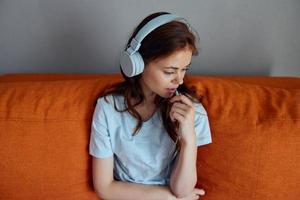 alegre mujer sentado en el sofá a hogar escuchando a música en auriculares apartamentos foto