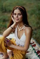 Young beautiful hippie woman sitting on the ground in nature in the fall in eco clothing in the sunset light, a lifestyle of travel and harmony with the world photo