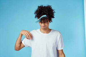 cute man with curly hair holding comb in hand and blue background cropped view photo