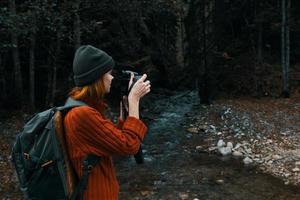 mujer con un cámara cerca un estanque en el montañas en naturaleza y arboles bosque paisaje foto