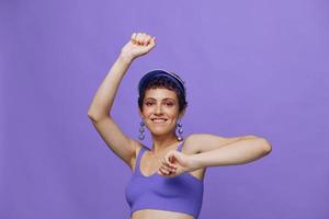 Deportes Moda mujer bailando posando sonriente con dientes en un púrpura Deportes traje para yoga en un esbelto cuerpo y un transparente gorra en su cabeza en un púrpura antecedentes monocromo foto