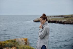 retrato de un mujer en un gris suéter soportes en un rocoso apuntalar naturaleza estilo de vida foto