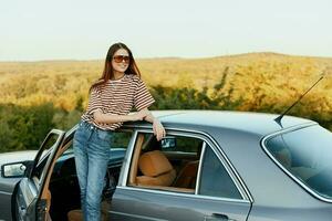 un joven mujer conductor mira fuera de el coche a el otoño paisaje y sonrisas satisfactoriamente foto