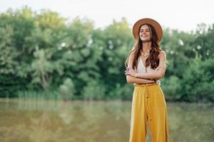 A young woman in a hippie look travels in nature by the lake wearing a hat and yellow pants in the fall photo