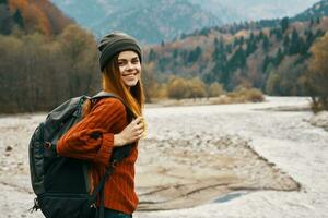 woman in a sweater hat with a backpack resting near the river in the mountains on nature landscape photo